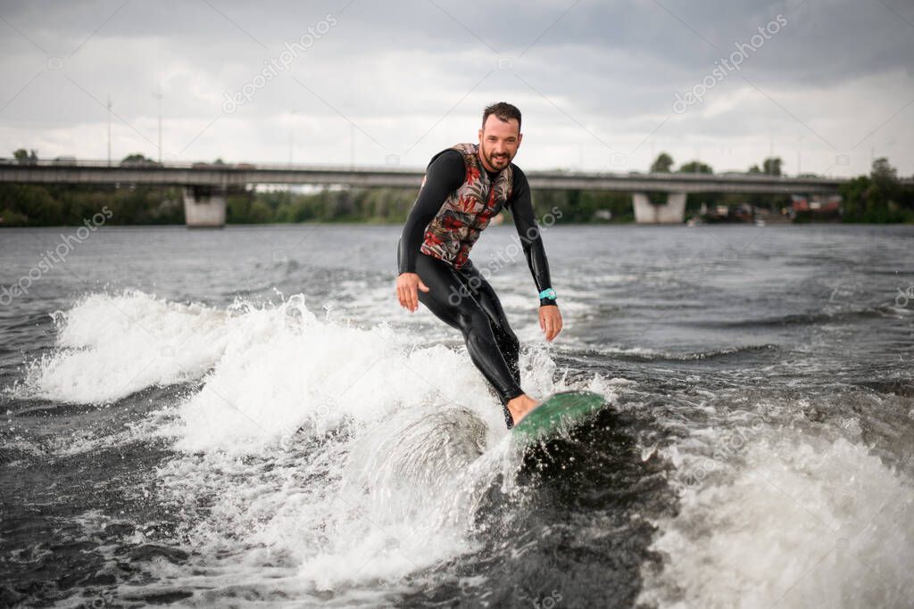 Smiling man is surfing on surfboard trails behind boat.