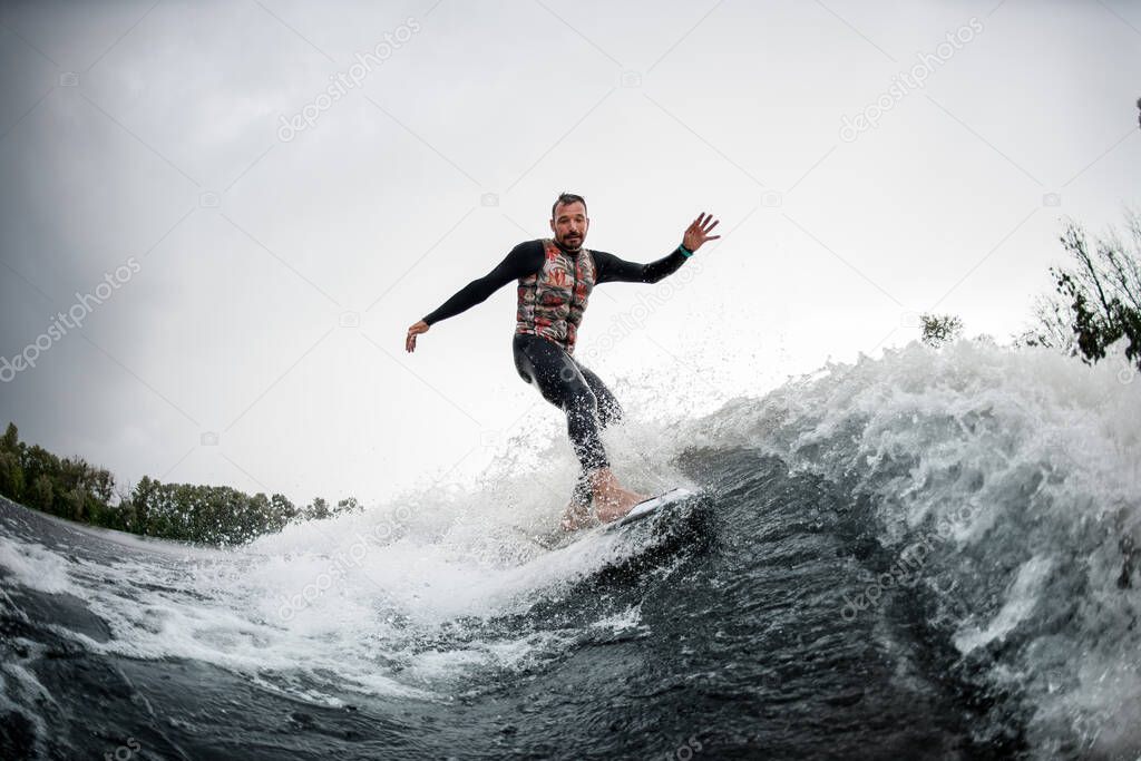 Active man in black swimsuit rides through the waves on water board