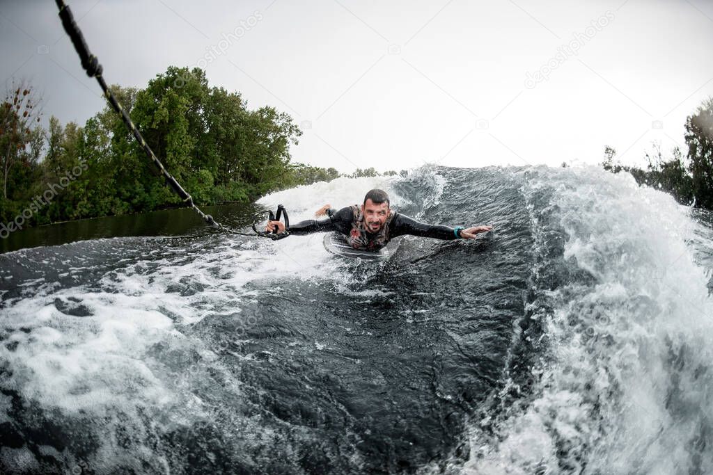 man holding rope and lying on wake surfboard rides on wave from motor boat
