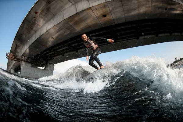 Deportista alegre wakesurfer en traje de neopreno en paseos de tabla de surf en la ola. —  Fotos de Stock