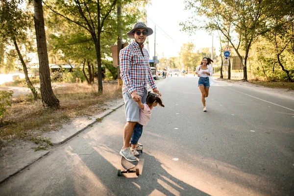 男は公園の路上で娘とスケートボードに乗っています — ストック写真