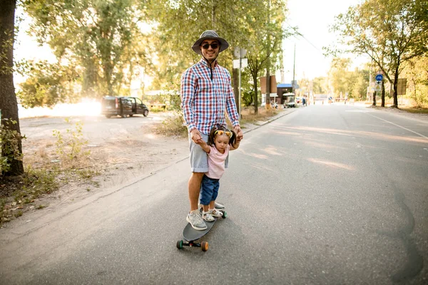 Homem junto com sua filha montando skate na estrada no parque — Fotografia de Stock