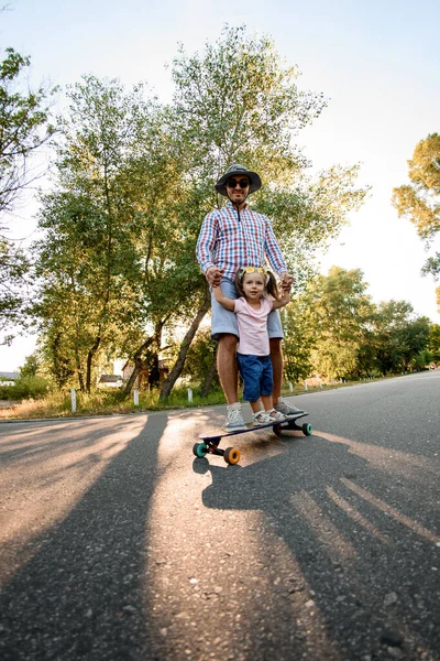 Jonge man met klein meisje oefenen skateboarden in park. — Stockfoto