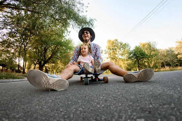 Pai alegre descansando sentado no skate com sua filha — Fotografia de Stock