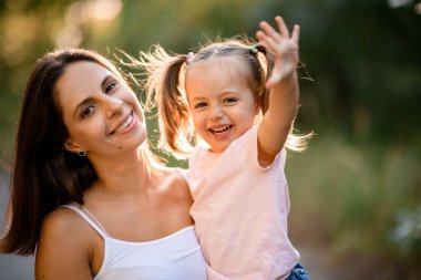 Genç, gülümseyen anne kollarında at kuyruklu küçük mutlu kız.