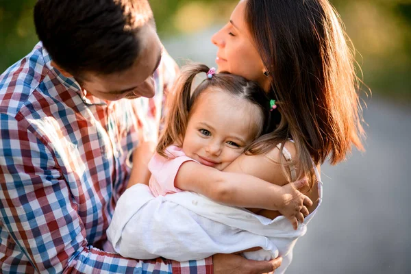 Heureux jeune familyhug leur petite fille charmante avec des queues de cheval sur sa tête — Photo