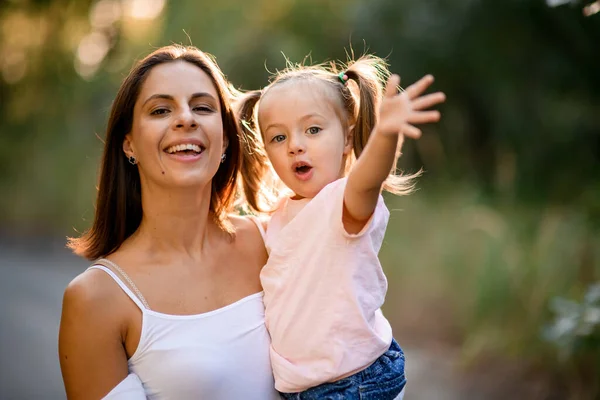 Jonge moeder houdt in haar armen kleine mooie meisje met paardenstaarten — Stockfoto