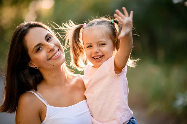 Genç, gülümseyen anne kollarında at kuyruklu küçük mutlu kız.