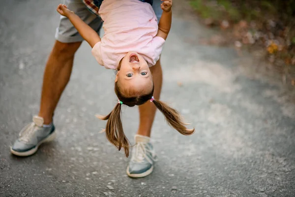 Blick auf das Gesicht eines glücklichen Mädchens in rosa T-Shirt, das ihr Vater auf den Kopf stellt und ihr schwingt — Stockfoto