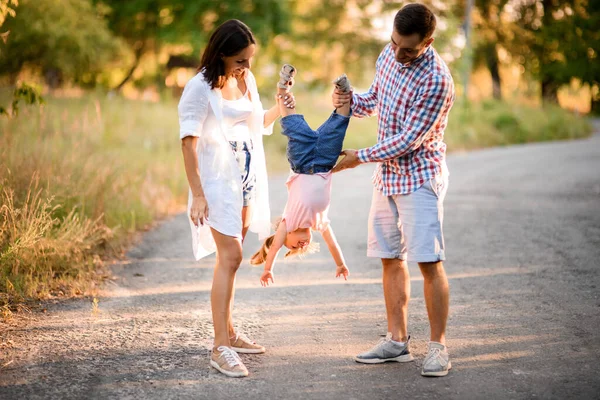 Unga föräldrar leker med sin lilla dotter och håller henne upp och ner. — Stockfoto