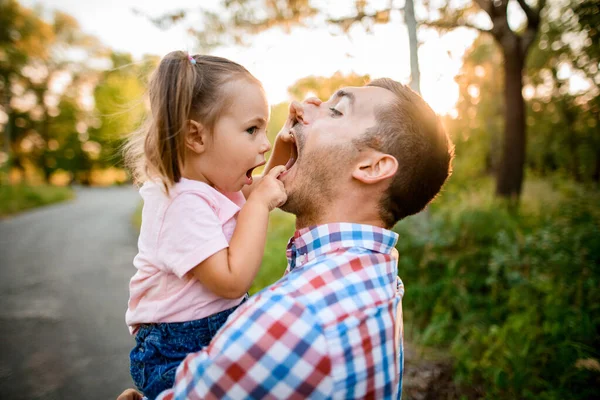 Šťastná malá roztomilá dívka sedí v náručí svého otce a baví — Stock fotografie