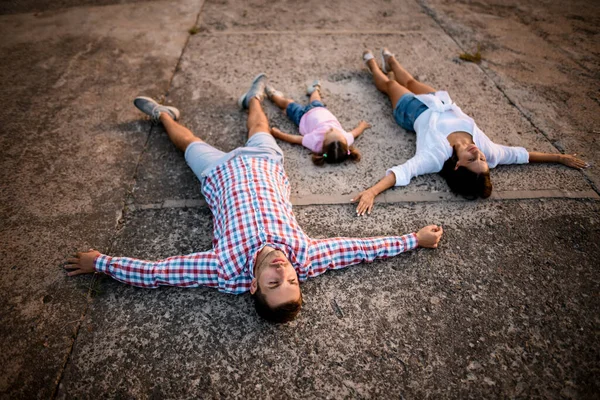 Jovem homem e mulher e menina jazem ao lado uns dos outros em asfalto cinza — Fotografia de Stock