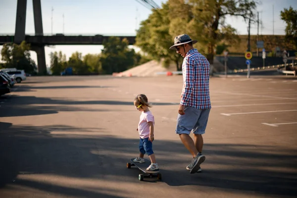 Vista de menina cavalgando skate enquanto seu pai caminha ao lado — Fotografia de Stock