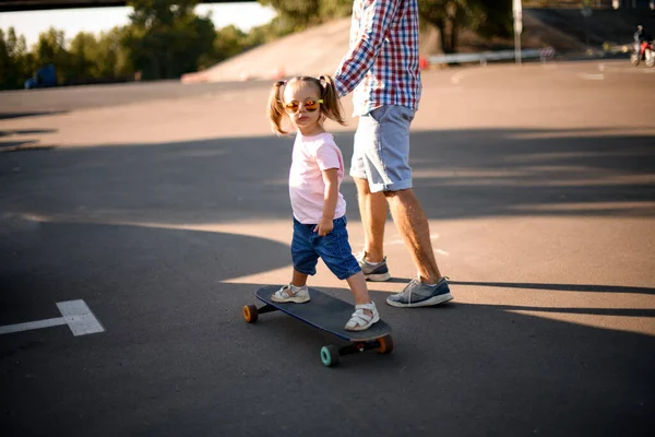 Vue rapprochée de la petite fille chevauchant le skateboard pendant que son père marche à côté — Photo