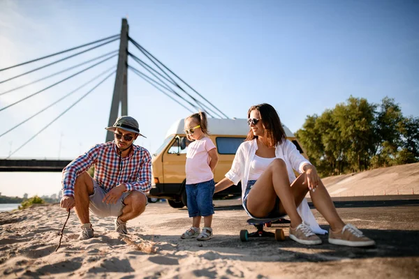 Szczęśliwa rodzina z małym dzieckiem spoczywa na piaszczystym brzegu rzeki — Zdjęcie stockowe