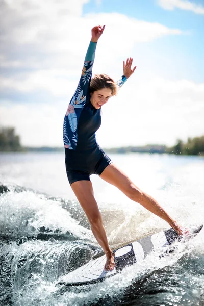 Primer plano de la mujer joven equilibra elegantemente en la tabla de surf montando la ola. —  Fotos de Stock
