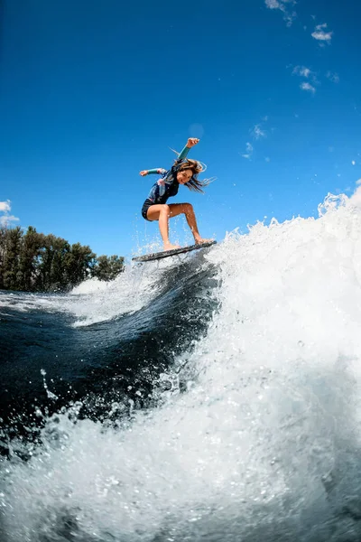 Hermosa mujer joven saltando hábilmente con tabla de surf en la ola —  Fotos de Stock