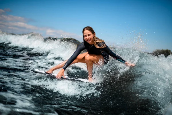 Fille souriante s'amuser assis sur la planche de surf et toucher l'eau avec sa main. — Photo