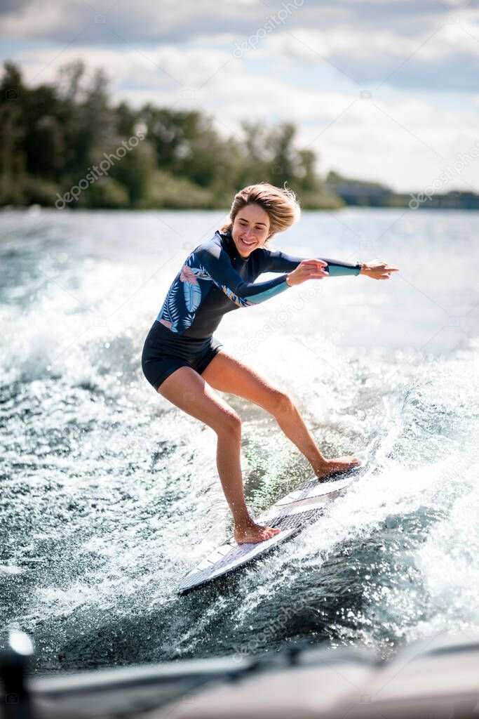 active woman riding surf board on the wave from motor boat