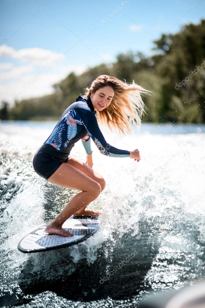 Beautiful woman stands with bent knees on surfboard and ride down on the splashing wave