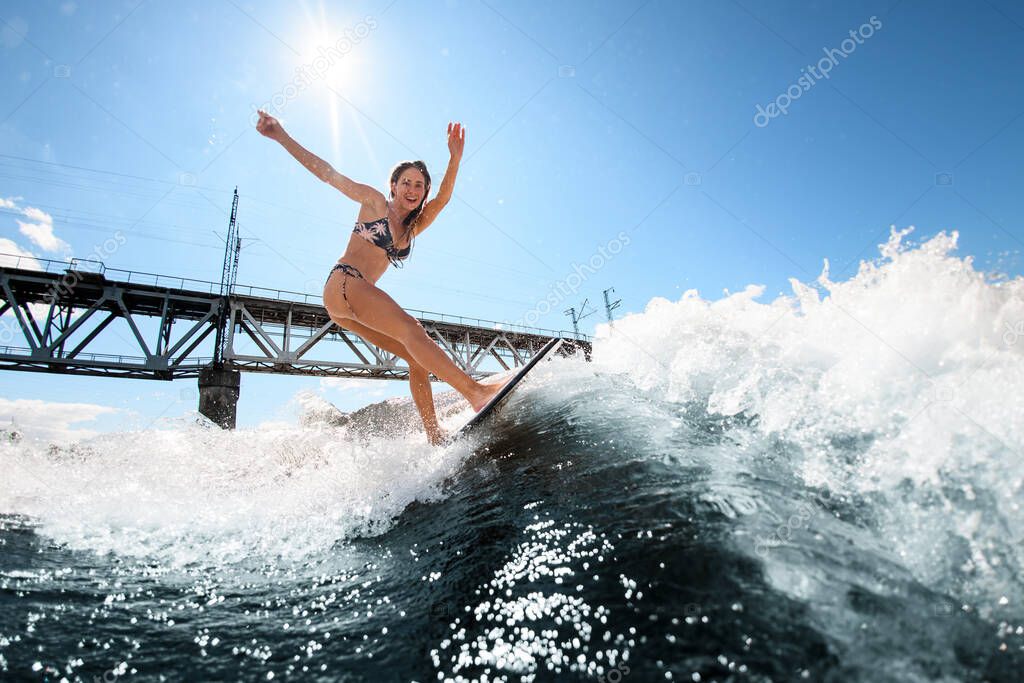 sporty woman on surfboard rides up the wave against the background of the bridge