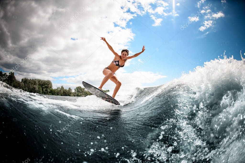 active young woman effectively jumps on the wave on surfboard