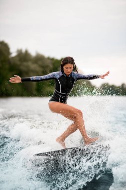 Sörf tahtasında dizleri bükülmüş ve su sıçratan dalgalarda dengede duran aktif bir kadın.