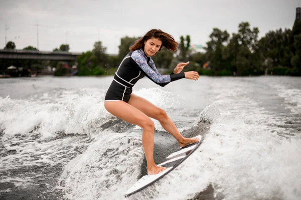 Aktive junge Frau im schwarzen Badeanzug reitet auf Surfbrett auf der Welle. — Stockfoto