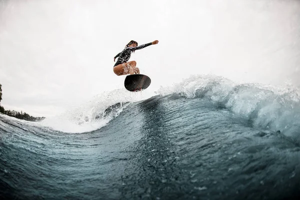 Joven mujer activa surfea fríamente en tabla de surf y salta en la ola —  Fotos de Stock