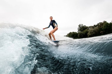 Dalgıç kıyafetli gülümseyen kadın dalgalar üzerinde sörf stili Wakeboard 'a biniyor.