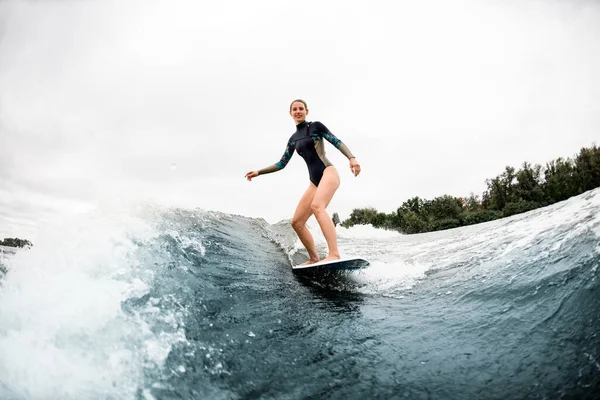 Sportliche Frau steht auf Wakeboard im Surfstil und reitet auf der Welle. — Stockfoto