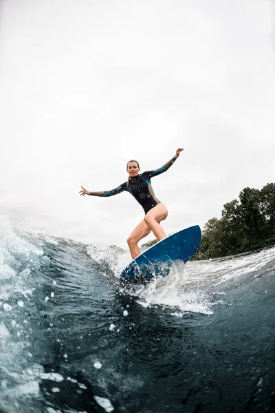 Aktive Frau steht mit gebeugten Knien auf Surfbrett und reitet auf Welle — Stockfoto