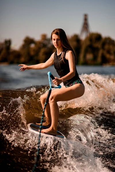 Junge Frau hält Seil mit und reitet auf dem Wakesurfbrett die Welle hinunter. — Stockfoto