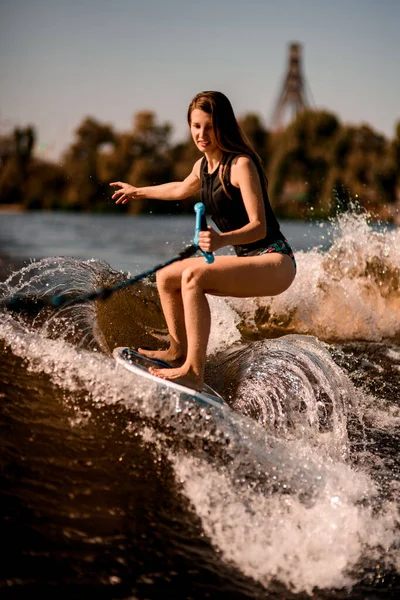 Nahaufnahme einer Frau, die mit gebeugten Knien auf dem Wakeboard steht und auf der plätschernden Welle hinunterreitet — Stockfoto