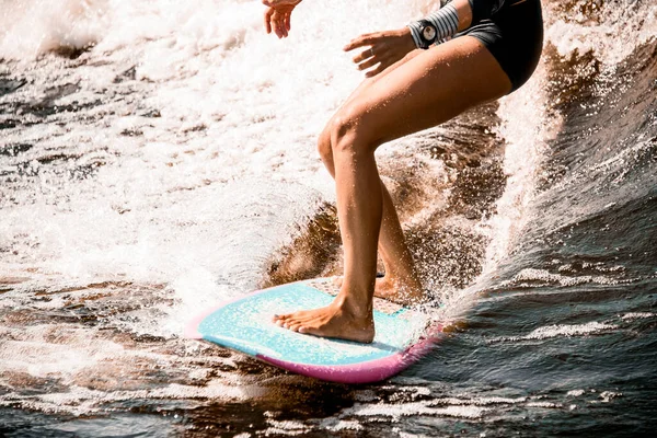 Nahaufnahme der athletischen Beine einer jungen Frau, die auf einer Welle auf einem Wakeboard im Surfstil reitet — Stockfoto