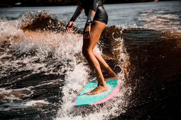 Uitzicht op gebruinde benen van vrouw paardrijden golf op surf stijl wakeboard — Stockfoto