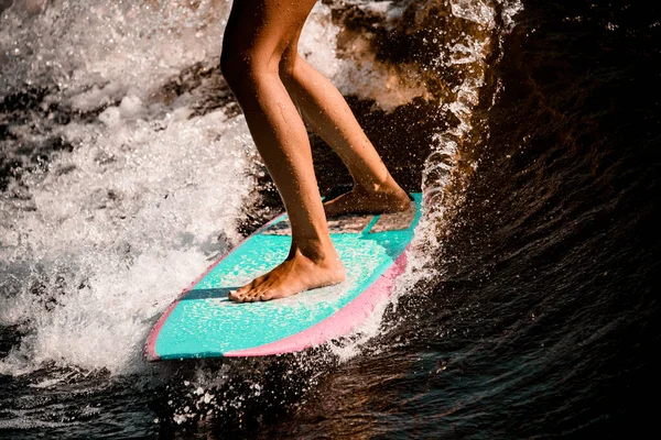 Close-up de belas pernas bronzeadas de mulher cavalgando onda no wakeboard estilo surf — Fotografia de Stock