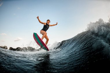 Neşeli kadın parlak sörf stili Wakeboard 'un üzerinde duruyor ve suyun üzerinden atlıyor.