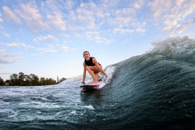 Gülümseyen genç bir kadın dizleri bükük sörf stili Wakeboard 'da oturur ve dalgalar üzerinde sörf yapar.