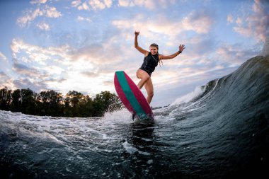 Enerjik genç bir kadın sörf stili Wakeboard 'un üzerinde duruyor ve dalgaların üzerinde aşağı iniyor.