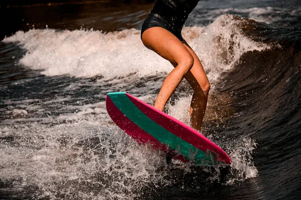 Nahaufnahme schöner braun gebrannter Beine einer Frau, die auf einer Welle auf einem Wakeboard im Surfstil springt — Stockfoto