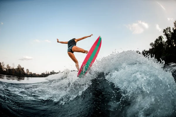 Chica activa en wakeboard estilo surf brillante y salta sobre salpicaduras de agua del río —  Fotos de Stock