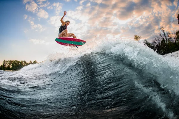 Vista sobre bela jovem mulher habilmente saltar sobre grande onda salpicando no wakeboard estilo surf. — Fotografia de Stock