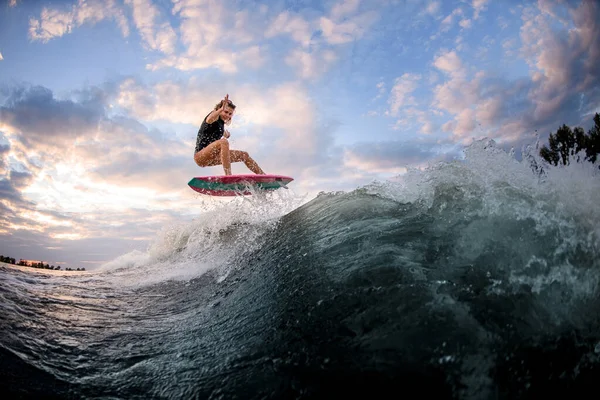 Atlética joven mujer en traje de baño saltando en el wakeboard estilo surf contra el cielo azul nublado —  Fotos de Stock