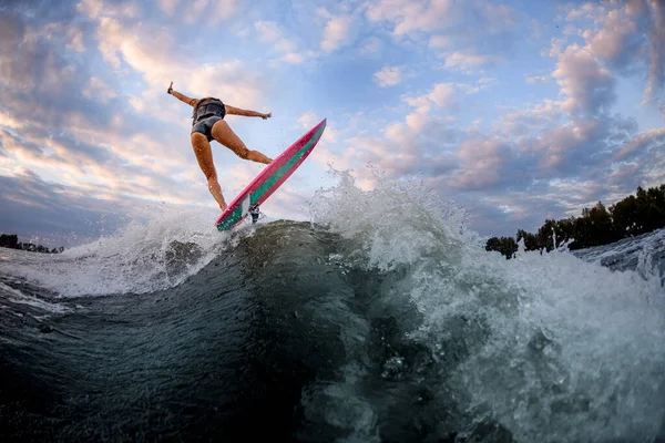 Hátsó kilátás a fiatal vonzó nő, aki áll a szörf stílusú wakeboard és ugrik a hullám. — Stock Fotó