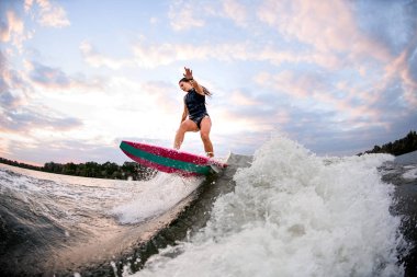 Sörf stilinde genç atletik bir kadın Wakeboard ve büyük bir su sıçrama dalgası üzerinde dengesi var.