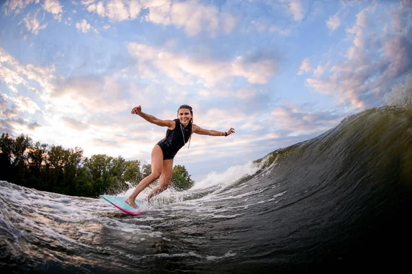 Sonriente joven mujer de pie en el wakeboard estilo surf brillante y paseos por la ola de agua grande —  Fotos de Stock