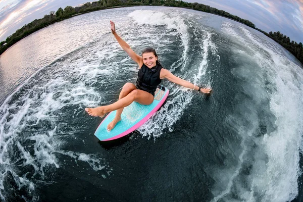 Vue grand angle d'une femme joyeuse assise sur un wakeboard de style surf et chevauchant la vague. — Photo