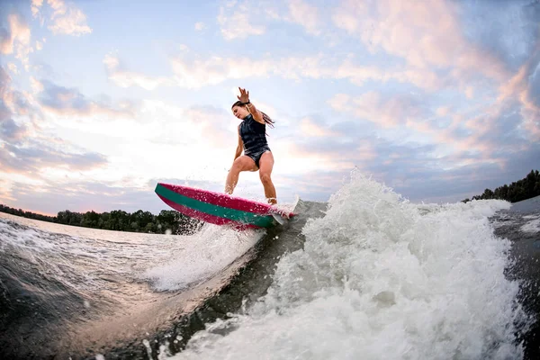 Young athletic woman on surf style wakeboard and balances on big splashing wave — Stock Photo, Image