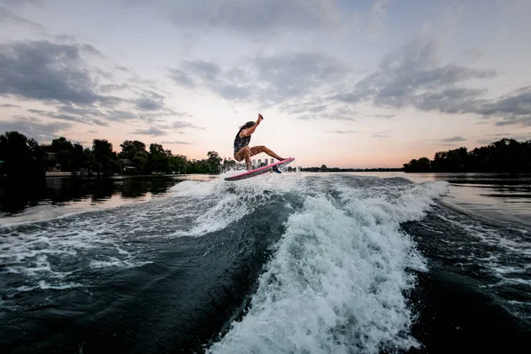 Vista na mulher atlética ativa pulando sobre onda salpicando no wakeboard estilo surf. — Fotografia de Stock